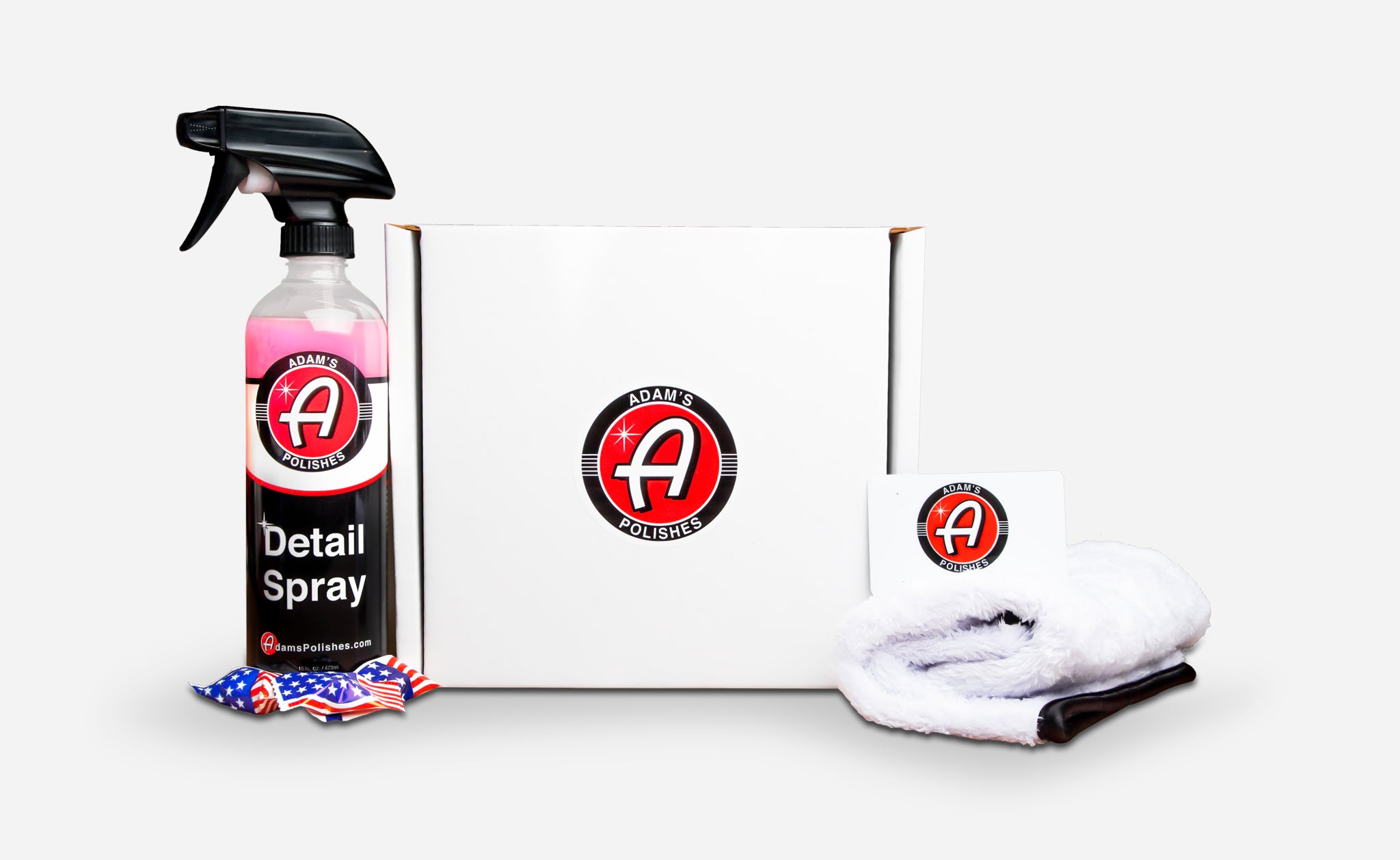Alt text: "Adam's Polishes $100.00 gift card box set, including a bottle of detail spray, a microfiber towel, and a gift card, all displayed against a white background with an American flag-themed air freshener."
